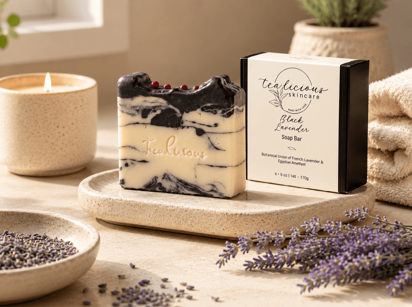 Tealicious Skincare Black Lavender Soap Bar with a cream and black marble pattern and small red berry accents, displayed next to its black and cream packaging box on a stone tray with lavender and a lit candle in a cozy setting.