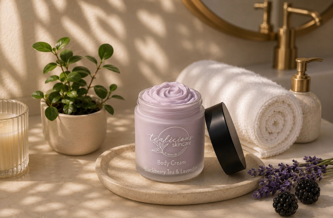 Tea-licious Skincare Blackberry Tea & Lavender body cream on a bathroom vanity with rolled towel, candle, and soft morning light.