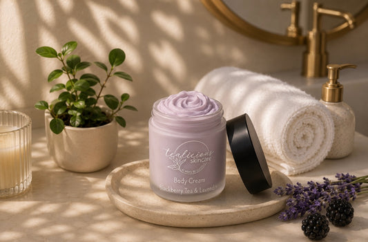Tea-licious Skincare Blackberry Tea & Lavender body cream on a bathroom vanity with rolled towel, candle, and soft morning light.