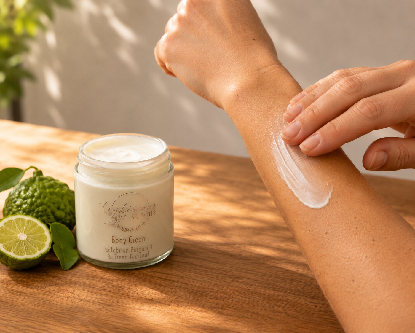 Tea-licious Skincare Calabrian Bergamot & green tangerine Tea body cream in a glass jar, styled with fresh bergamot and dried tea leaves on a wooden surface in soft morning light.