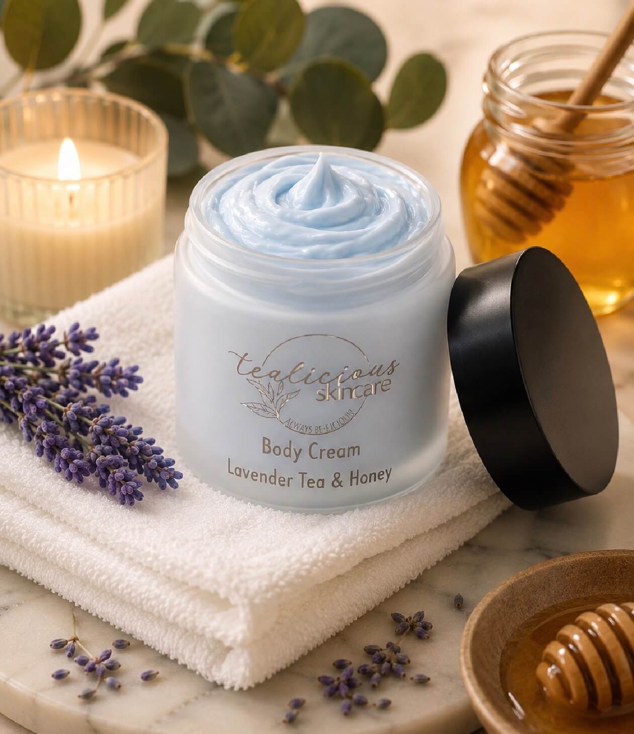 Tea-licious skincare body cream with lavender, tea, and honey on a marble surface with a candle and honeycomb.