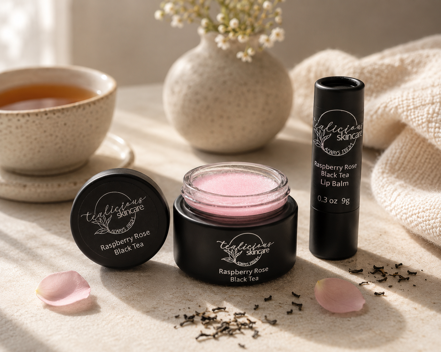 Tea-licious Skincare lip balm tubes resting on a soft surface with a cup of tea and dried flowers. This professional homestyle image highlights the botanical-inspired ingredients and anhydrous formulation in soft, natural morning light.
