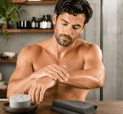 Sophisticated man applying Tea-Licious men’s solid lotion bar to his forearm in a modern bathroom, showing real skin texture and healthy moisturized skin with a masculine grooming routine.