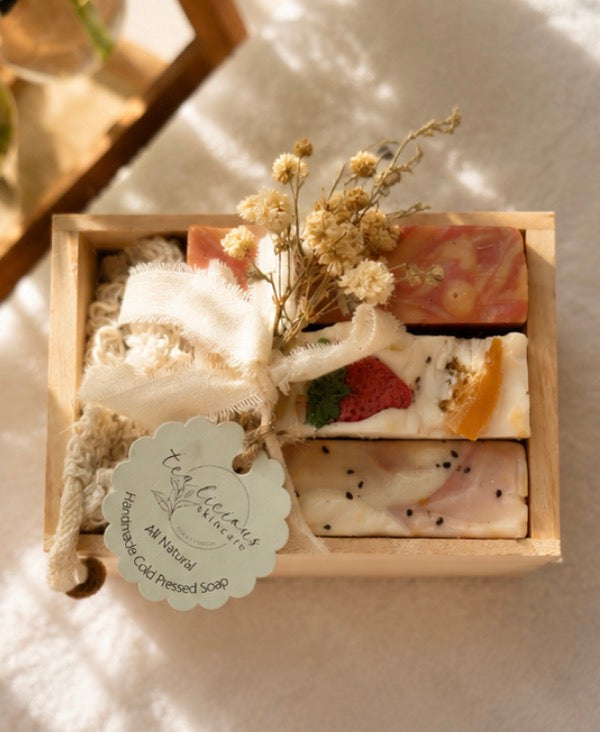 Three Tea-licious artisan soap gift sets displayed on wooden stand with botanical decor.