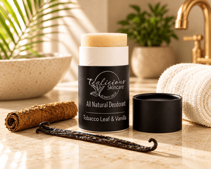Tea-licious Black Tea & Sandalwood deodorant beside a rolled white towel, steaming black cup and mound of brown powder on a sunlit wooden surface.