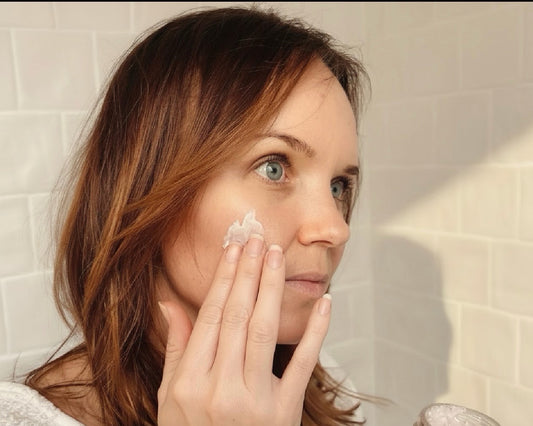 Woman applying White Guava Tea Moisture Infusion cream in soft natural bathroom morning light.