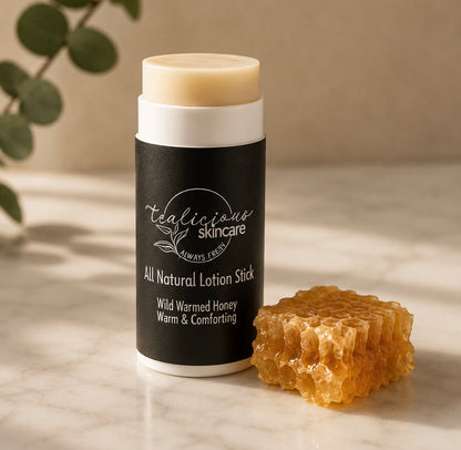 Tea-licious Skincare Wild Warmed Honey lotion stick next to a piece of fresh honeycomb on a marble surface.