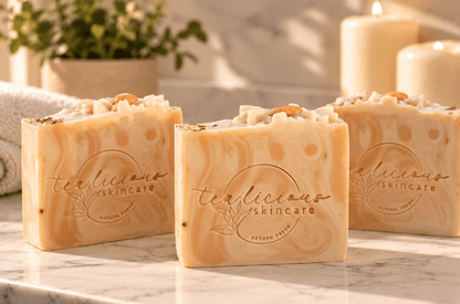 Three Tea-Licious handcrafted soap bars with creamy peach swirls displayed on a marble counter with candles and greenery in soft natural light.