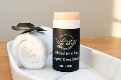 Tealicious Skincare Bergamot and Rose Lavender all-natural lotion stick on a white marble tray next to a rolled white towel and a eucalyptus leaf.